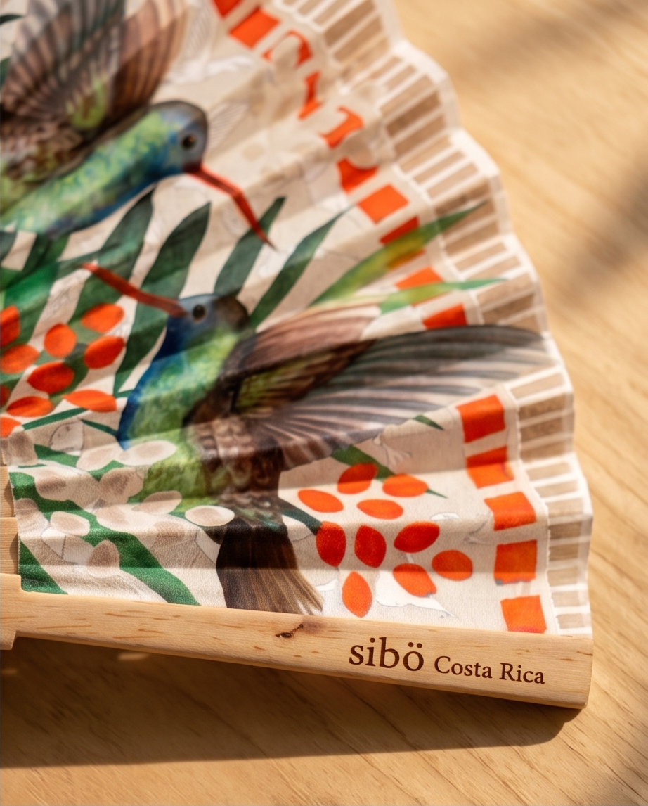 Wooden fan close up picture with colorful hummingbird design and 'sibo Costa Rica' branding on a wooden surface.