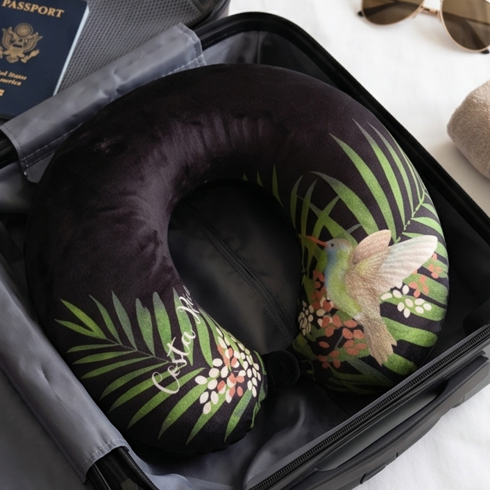 Neck pillow with tropical design in an open suitcase with a passport and sunglasses.