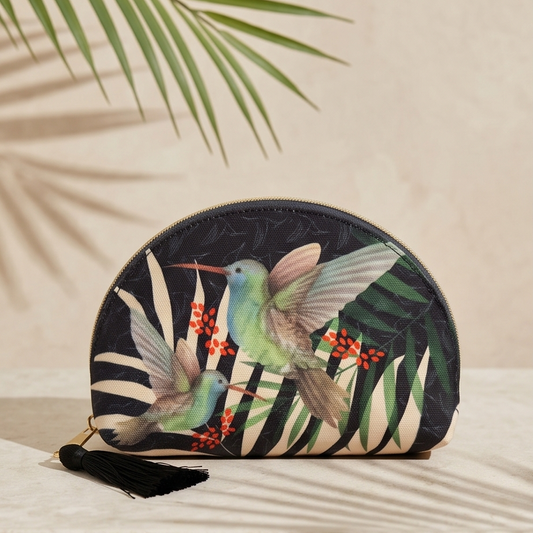 Round cosmetic pouch with hummingbird design on a beige surface with palm leaves in the background
