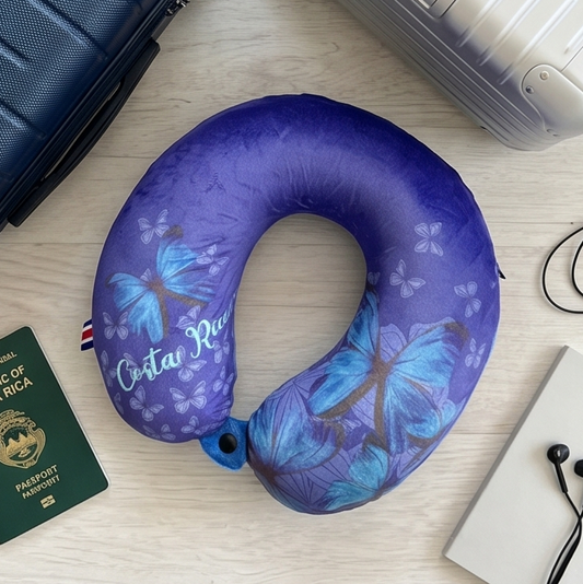Blue butterfly-patterned neck pillow with two suitcases and a passport on a light surface.