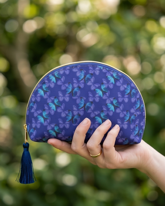 Hand holding a blue butterfly patterned pouch with a tassel against a blurred green background